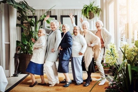 Ein Senior im Rollstuhl wird von einer Pflegerin entlang eines Rosenbeets geschoben.