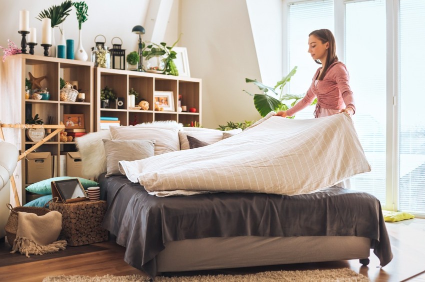 Frau Mitte 30 legt eine Decke über das Bett im Schlafzimmer.