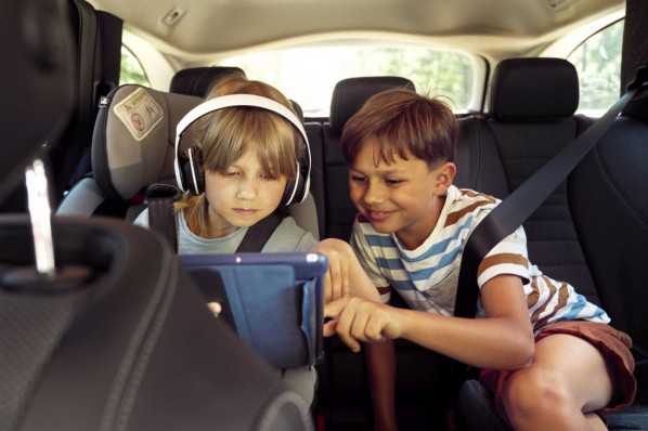 Zwei 7-jährige Jungen sitzen auf der Rückbank des Autos und spielen auf einem Tablet. 