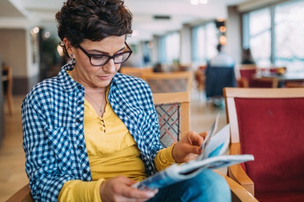 Eine etwa 45-jährige Frau blättert durch ein Magazin, während sie in einem Café sitzt.