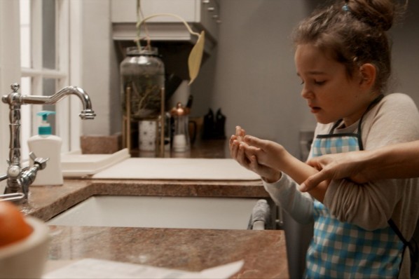 Ein etwa 7 jähriges Mädchen hat sich die Finger verbrannt und kühlt sie am Wasserhahn.