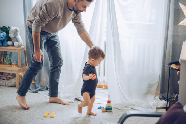 Kleinkind und Vater laufen barfuß im Kinderzimmer.