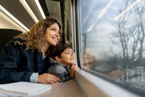 Junge Mutter sitzt mit ihrem Sohn am Zugfenster und betrachtet die Natur. 