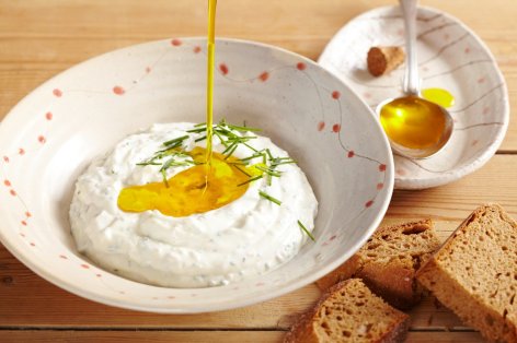 Auf einem Holztisch steht ein Teller mit Quark, auf den Leinöl gegossen wird. Daneben liegt selbst gebackenes, frisches Mehrkornbrot.