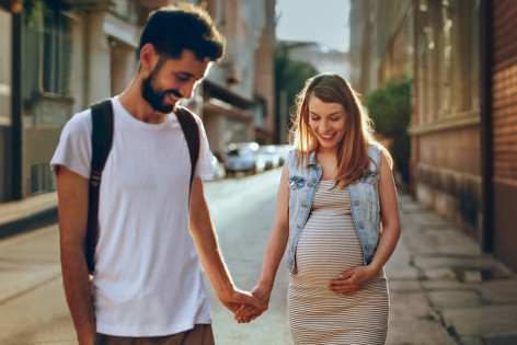 Paar erwartet Kind und spaziert händchenhaltend im Sonnenschein. - AOK Sachsen-Anhalt begleitet mit exklusiven Leistungen für werdende Eltern.