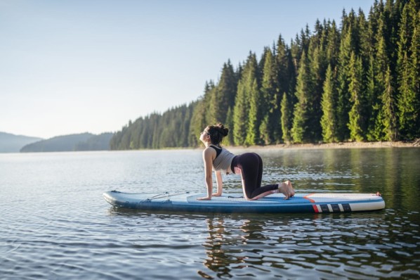 Ein Frau beim SUP-Yoga auf ihrem Board treibend.