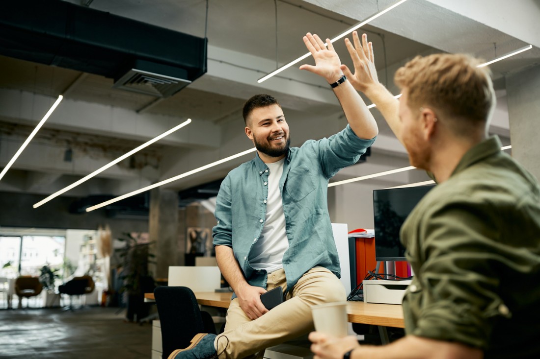 Happy entrepreneur and his colleague give high five while congratulating each other on well done job.