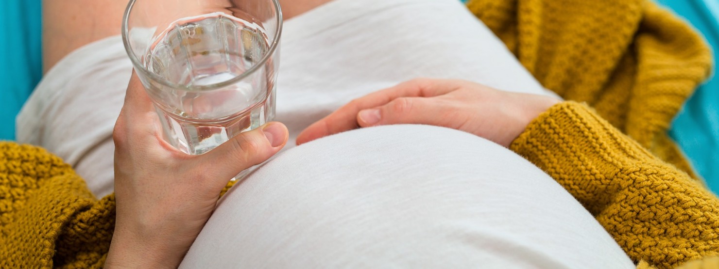 Schwangere hält ein Glas Wasser in der Hand
