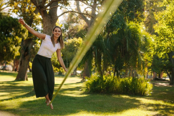 Eine gut gelaunte Frau balanciert über eine Slackline im Park