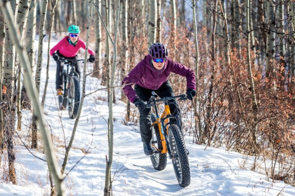Zwei Jugendliche fahren mit Mountainbikes durch den schneebedeckten Wald.
