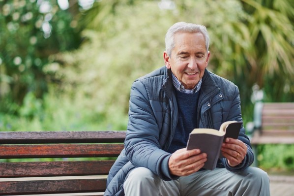 Ein etwa 60-jähriger Mann liest auf einer Parkbank ein Buch.