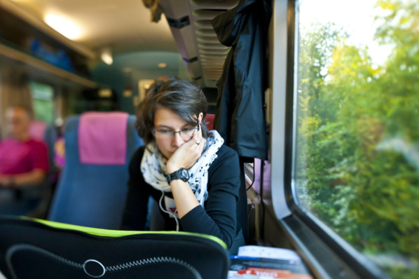 Eine etwa 25-jährige Frau sitzt arbeitenden an ihrem Laptop in einem Zug.
