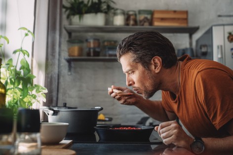 Junger mann in orangenem tshirt probiert Suppe aus einem flachen Topf 