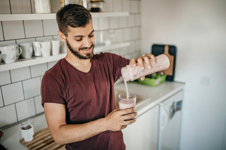 Ein junger Mann bereitet sich einen Smoothie mit einem Mixer zu.