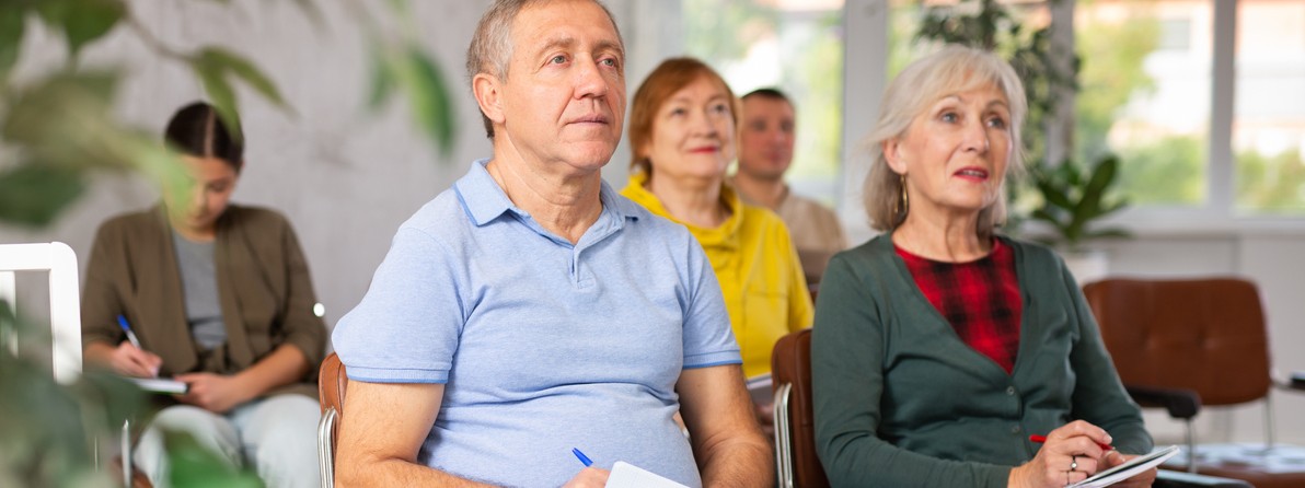Pflegende Angehörige hören bei einem Pflegekurs zu und machen sich Notizen.