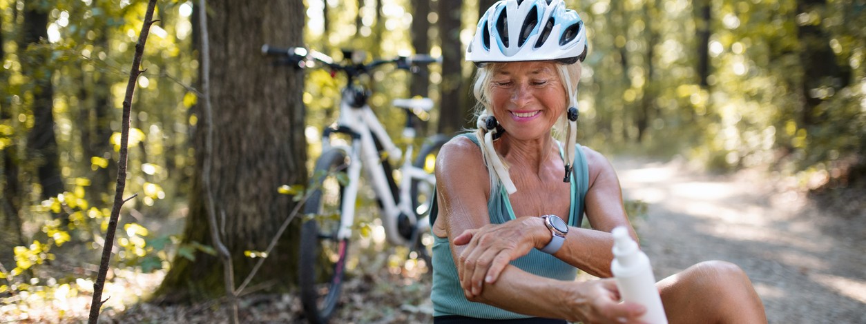 Eine Frau macht im Wald eine Pause vom Fahrradfahren und trägt Sonnenschutz auf