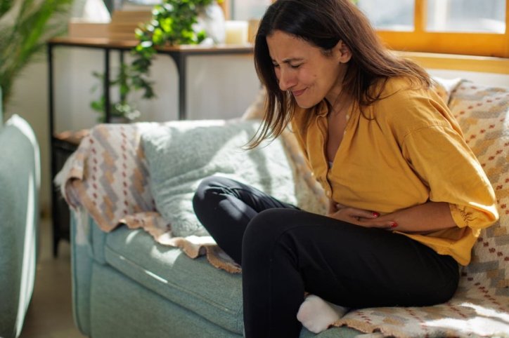 Eine Frau sitzt auf einem Sofa und verspürt starke Bauchschmerzen