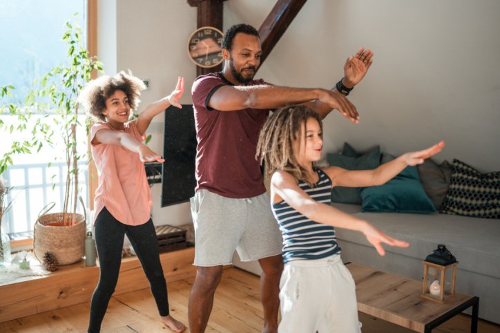 Eine Familie tanzt gemeinsam zuhause im Wohnzimmer.