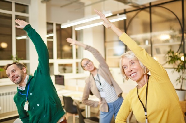 3 Kollegen, 1 mann und 2 Frauen, machen Dehnübungen im Büro.