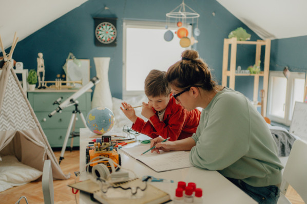 Mutter hilft ihrem kleinen Sohn in seinem Kinderzimmer bei den hausaufgaben