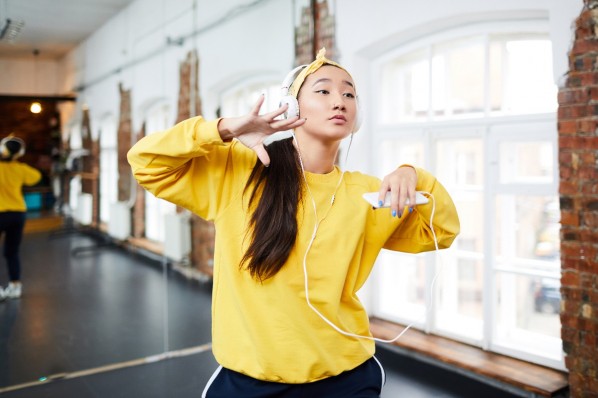 Eine etwa 25-jährige Frau tanzt mit Kopfhörern und Handy in der Hand Hiphop in einem Tanzstudio.