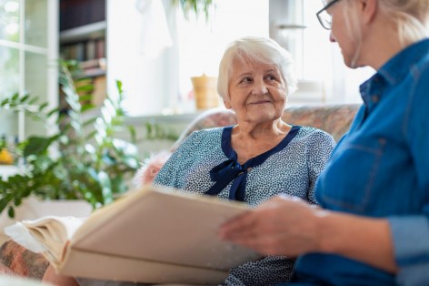 Etwa 70 jährige Frau schaut sich mit ihrer etwa 40 jährigen Tochter ein Fotoalbum an