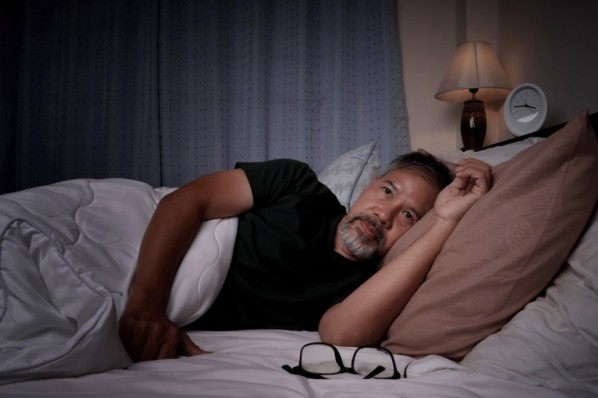 EIne junge Frau recherchiert im Bett liegend auf Ihrem Smartphone nach Ursachsen für Ihre Schlaflähmungen.