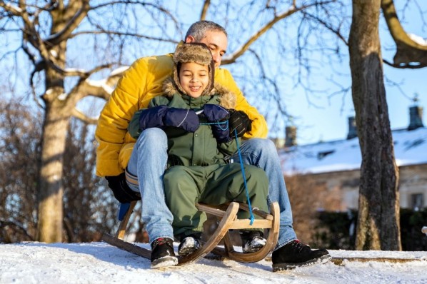 Ein vater sitzt zusammen mit seinem kleinen Sohn auf dem Schlitten und rodelt einen Hügel hinunter