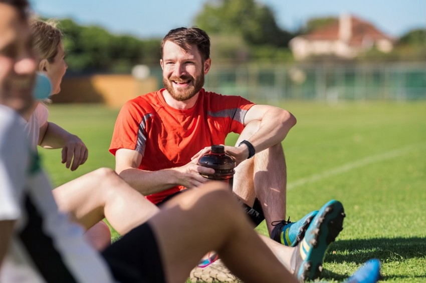 Ein etwa 35-jähriger Fußballer macht mit seinen Freunden eine Pause. Sie sitzen auf dem Spielfeld.