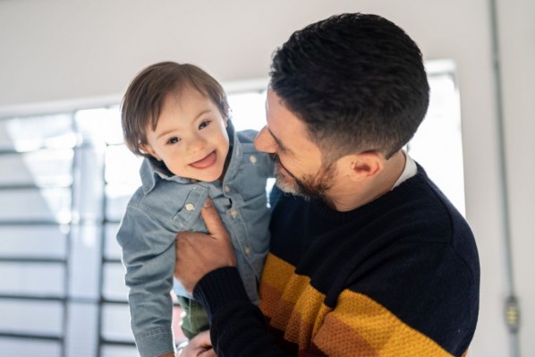 Ein Vater trägt seinen kleinen Jungen mit Down-Syndrom.