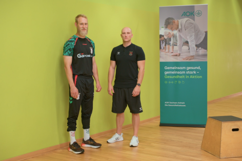 Ein Sporttrainer und ein Handballer schauen in die Kamera.