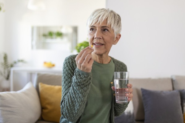 Senior woman takes pill with glass of water in hand.