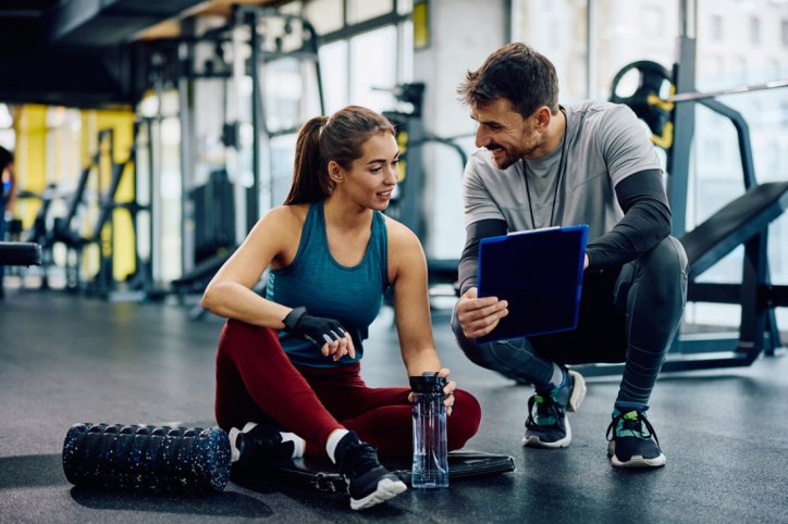 Ein Fitnesstrainer berät eine Frau in Sachen Hybrid-Training