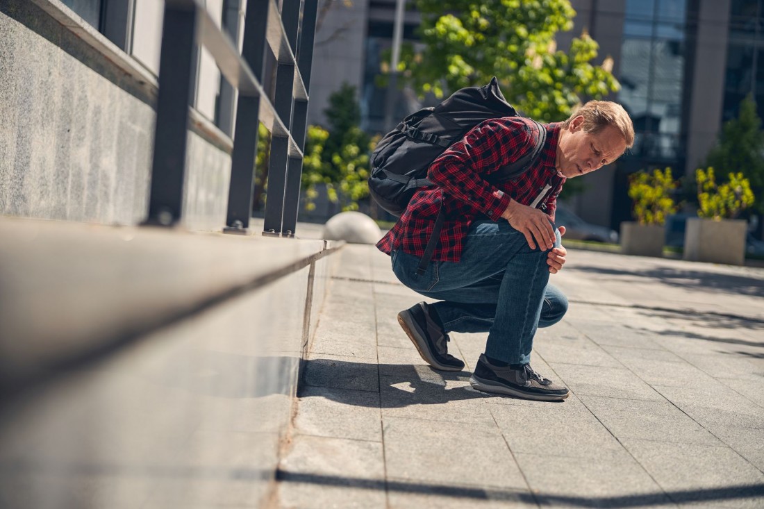 Mann mittleren Alters hält sein schmerzendes Knie auf dem Weg zur Arbeit.