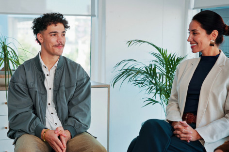 Ein etwa 25-jähriger Mann sitzt gemeinsam drei anderen Personen in einer Praxis zusammen. Alle Personen nehmen an einer Gruppentherapie teil und schauen sich an.