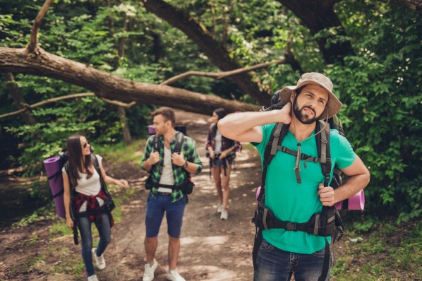 Vier etwa 30 jährige Personen laufen durch einen Wald. Der Mann im Vordergrund fest sich genervt an den Hals. Er wird von Mücken geplagt.