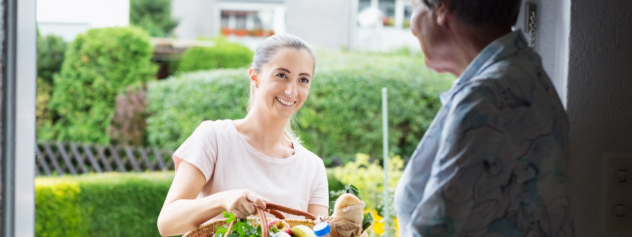 Eine Frau der Nachbarschafthilfe bringt einer Seniorin ihre Einkäufe