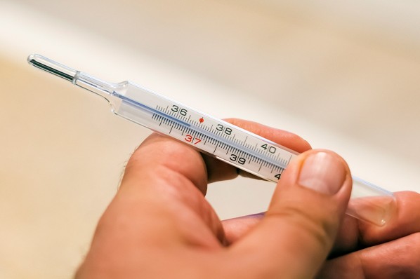 Eine Hand hält ein Fieberthermometer mit Quecksilber.