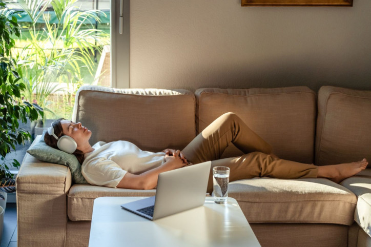 Eine Frau liegt auf der Couch. Sie hört eine Hypnose über ihre Kopfhörer.