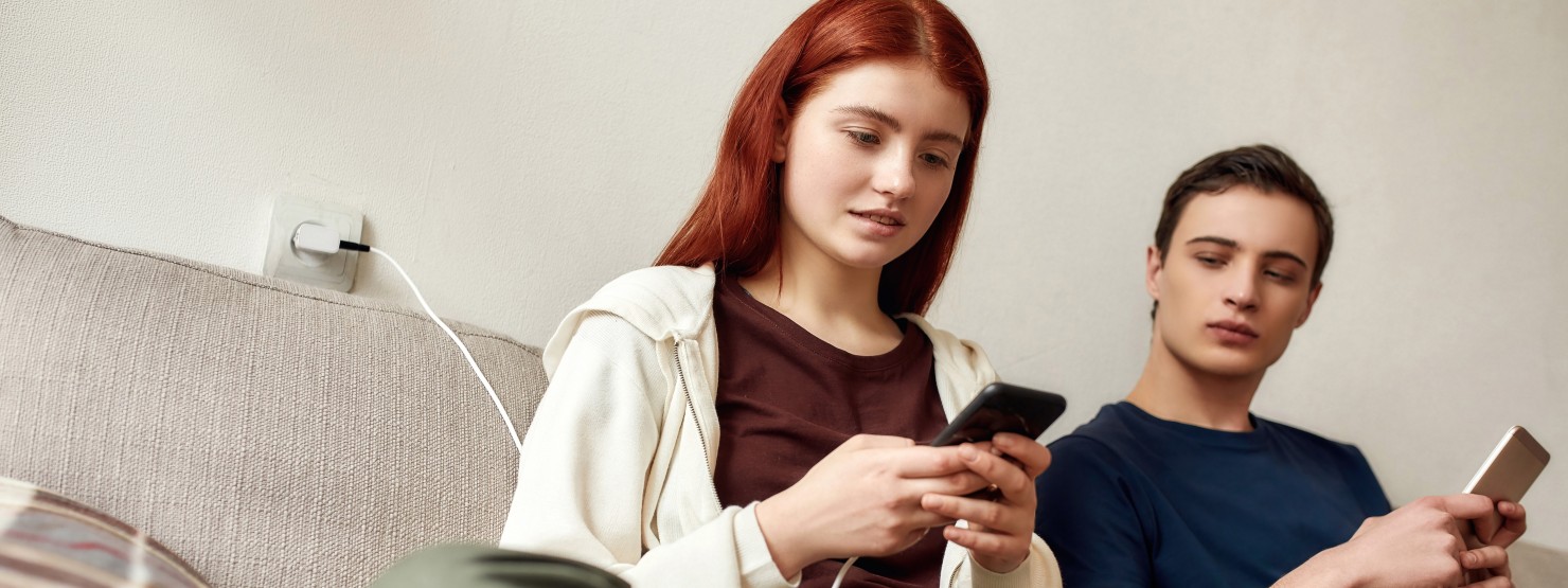 Zwei Teenager sitzen auf dem Sofa und schauen aufs Smartphone