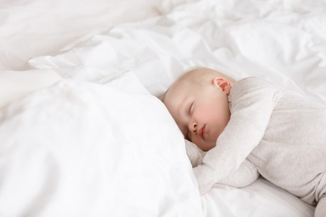 Kleinkind liegt im weißen Bett und schläft.