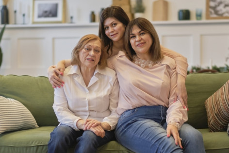 Drei Frauen aus unterschiedlichen Generationen sitzen gemeinsam lächelnd auf einer Couch.