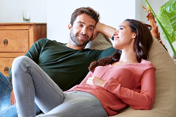 Junges Paar sitzt gemeinsam auf der Couch. Sie entspannen sich dabei. 