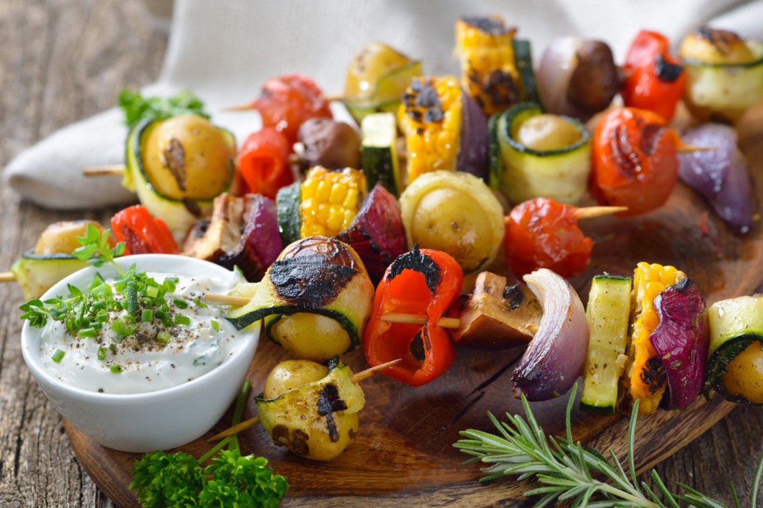 Gegrillte Spieße mit gemischtem Gemüse serviert auf einem Holzschneidebrett mit veganem Kräuterdip.
