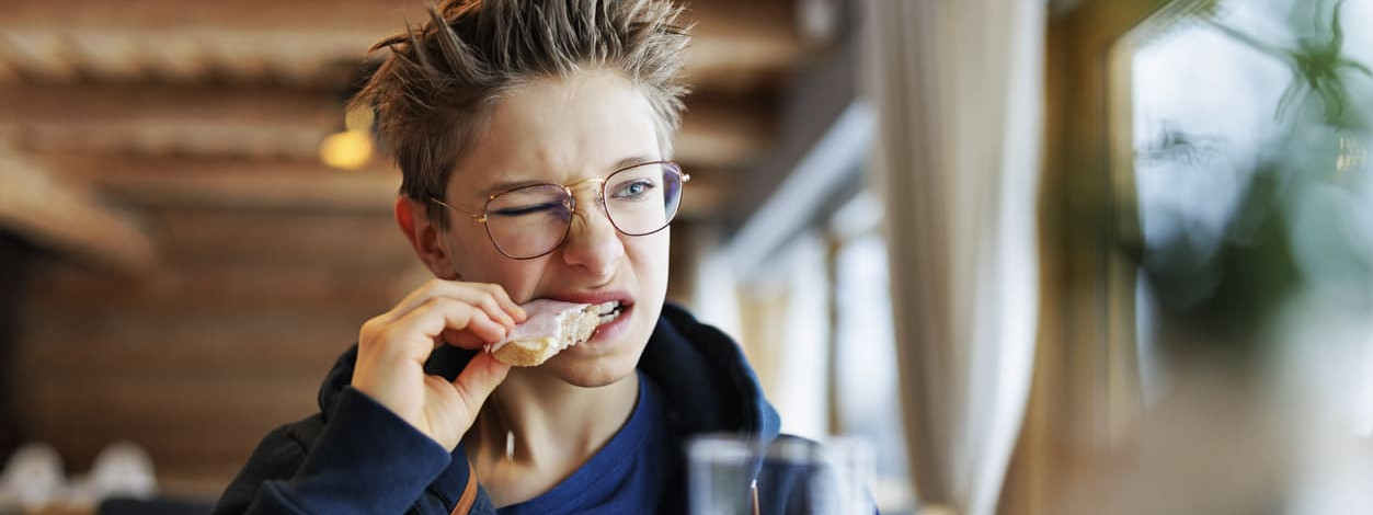 Ein Junge beißt etwas angewidert in ein belegtes Brot