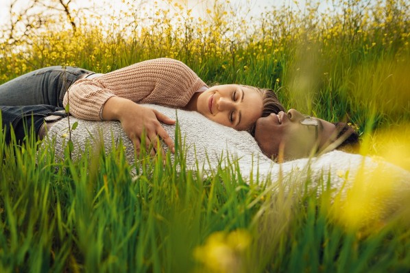 Ein etwa 30-jähriges Pärchen liegt mit geschlossenen Augen in einem Blumenfeld.