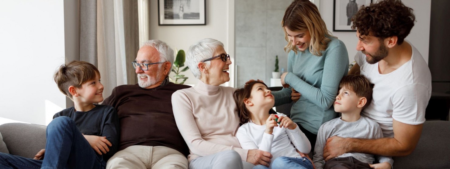 Eine 7-köpfige Familie mehrer Generationen sitzen gemeinsam auf einem Sofa und lachen.