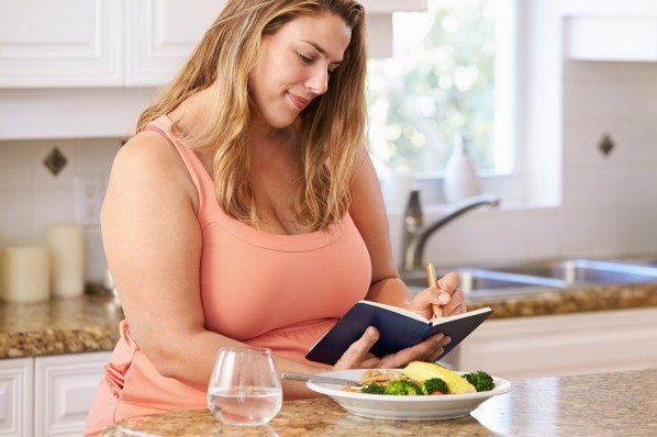 Übregewichtige Frau notiert ihre Diät-Erfolge in einem Ernährungstagebuch