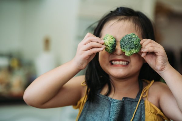 Ein junges Mädchen hält sich 2 Broccoli-Röschen vor die Augen