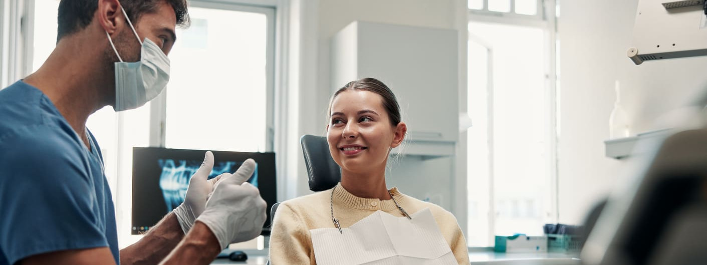 Ein freundlicher Zahnarzt erklärt einer Patientin auf dem Behandlungsstuhl sein Vorgehen.